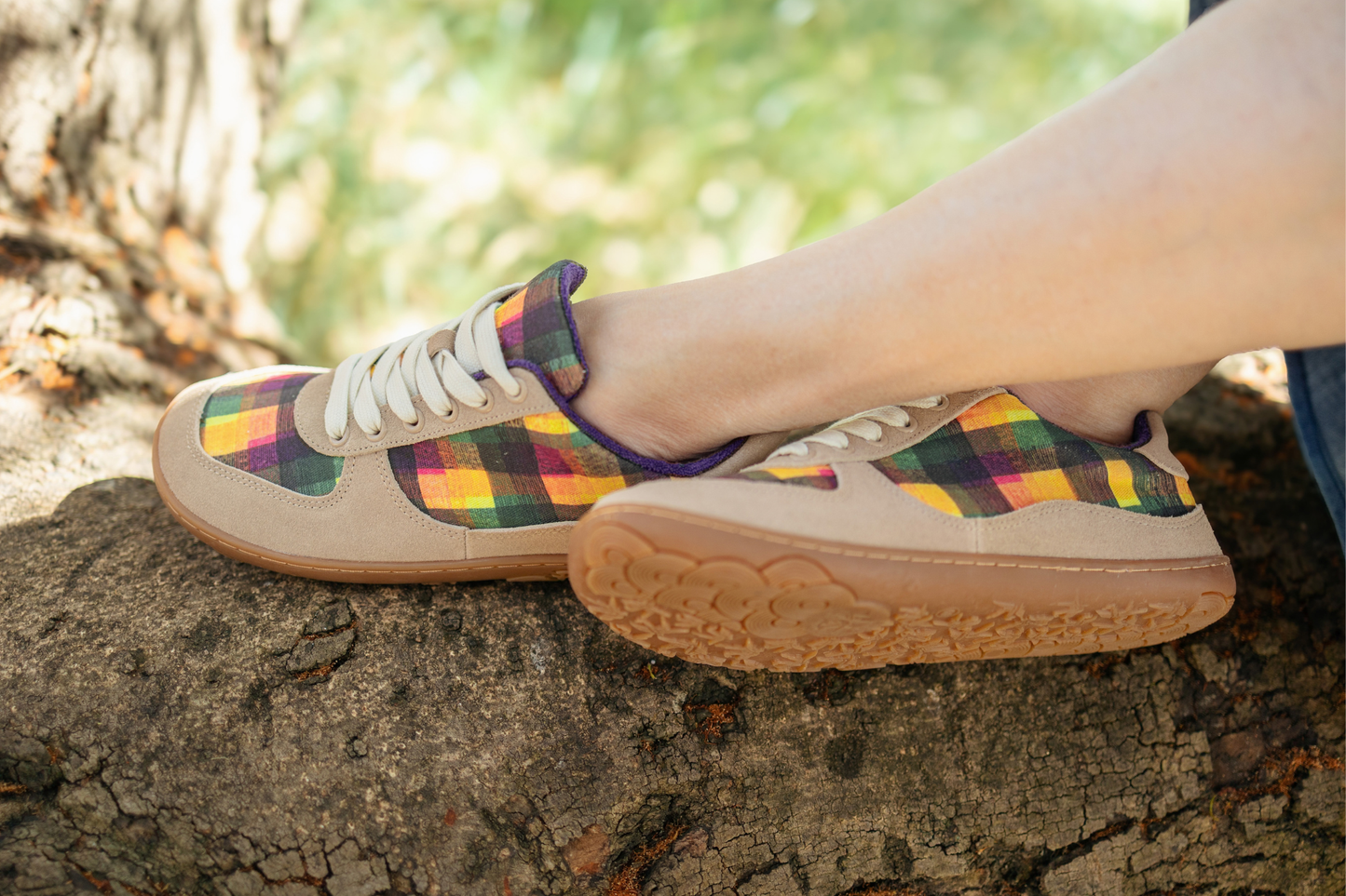 Colourful plaid sneakers with DI Nowinski checkered art print, tan suede, and gum sole on a person's feet, sitting on a tree branch in Australian bush setting.
