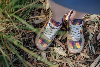 Colourful plaid print sneakers by PaperKrane and artist Di Nowinski viewed from above on a person standing in Australian grass and leaves