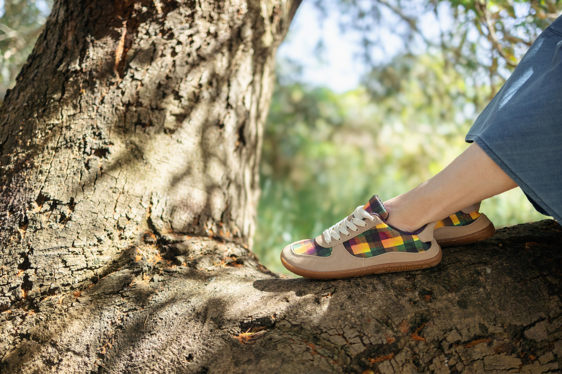 Person wearing colourful plaid print barefoot sneakers sitting on a tree branch with a natural background