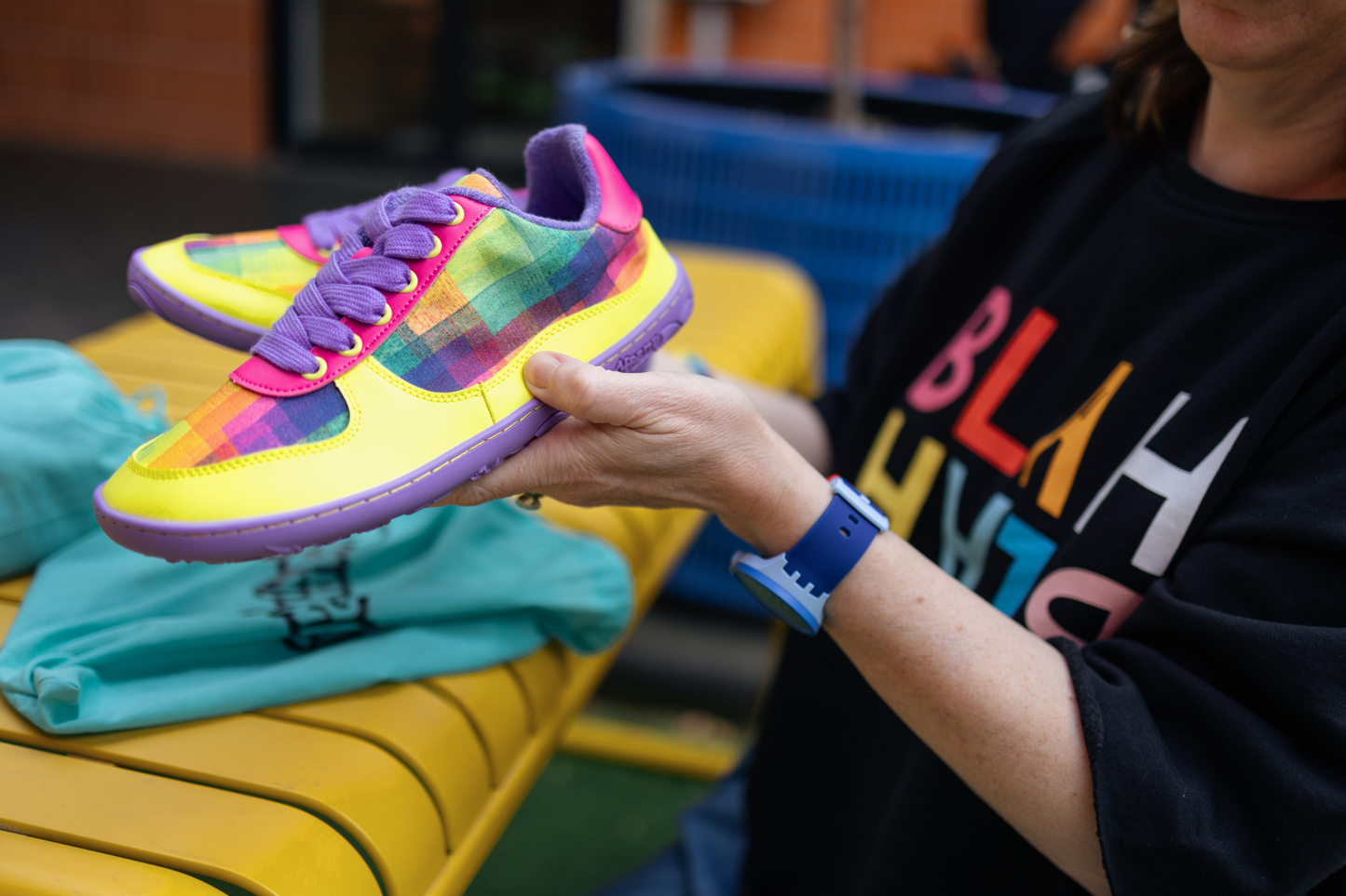 Di Nowinski holding a pair of colourful PaperKrane sneakers with a blurred background