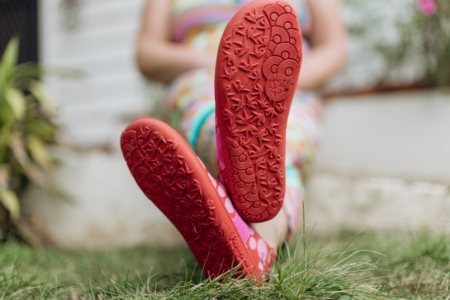 Close-up of red foot-shaped PaperKrane mary Jane shoes with textured soles on grass