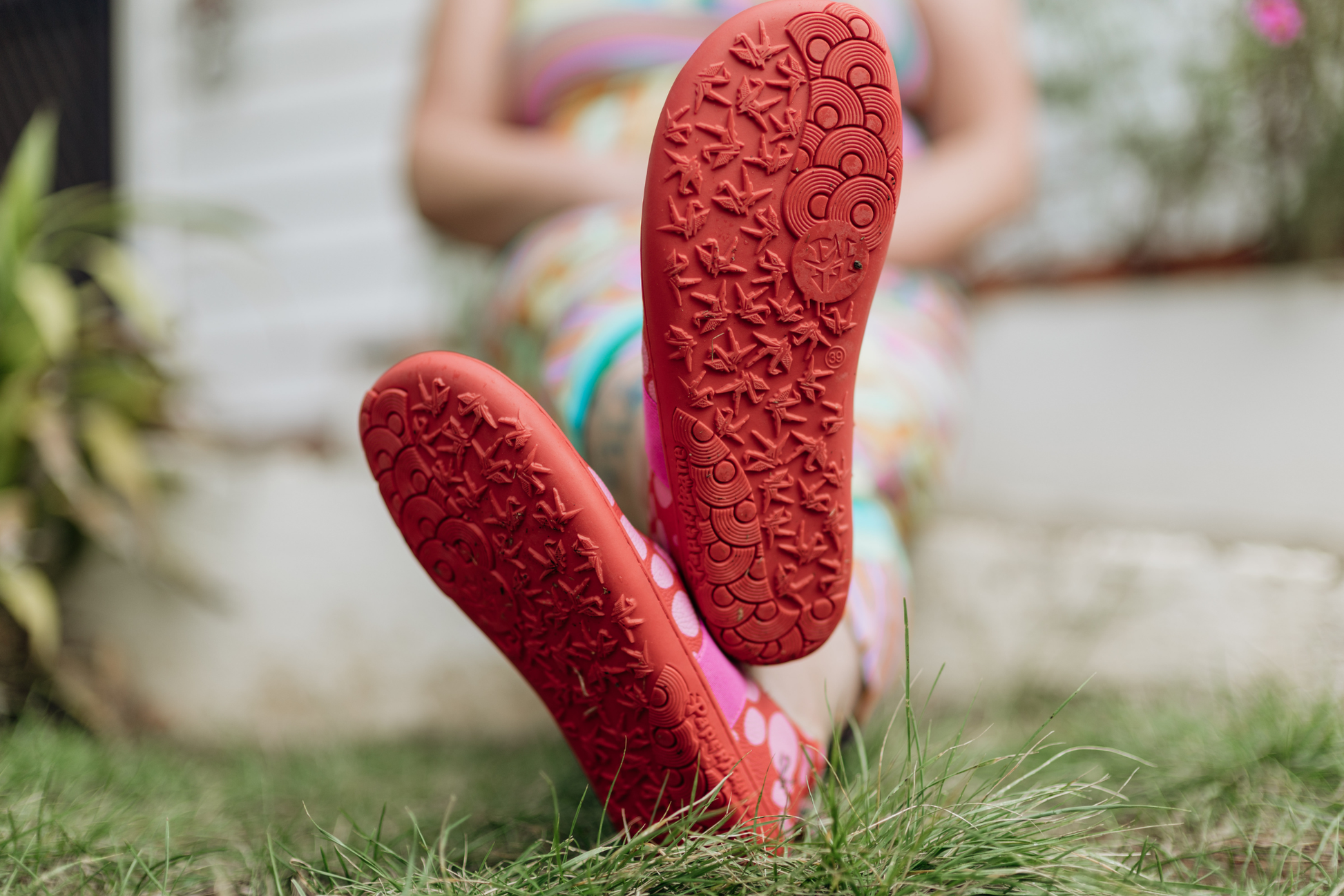 Close-up of red foot-shaped PaperKrane mary Jane shoes with textured soles on grass