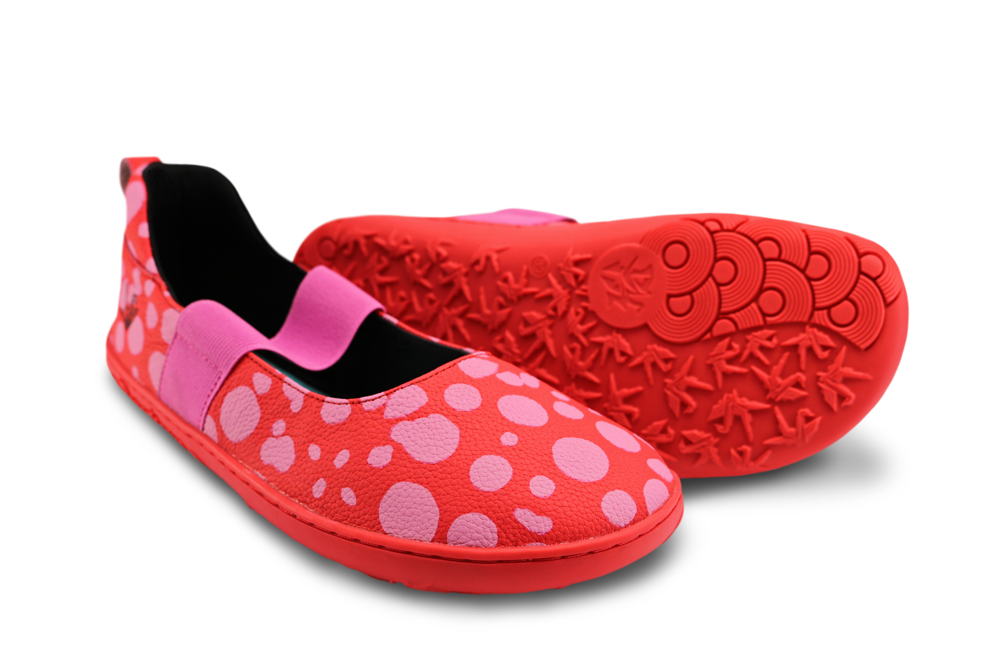 Red leather PaperKrane barefoot mary jane style shoe with bubblegum pink painted spots and pink elastic band, and red rubber soles. They're on an angle, one is showing its sole, on a white background.