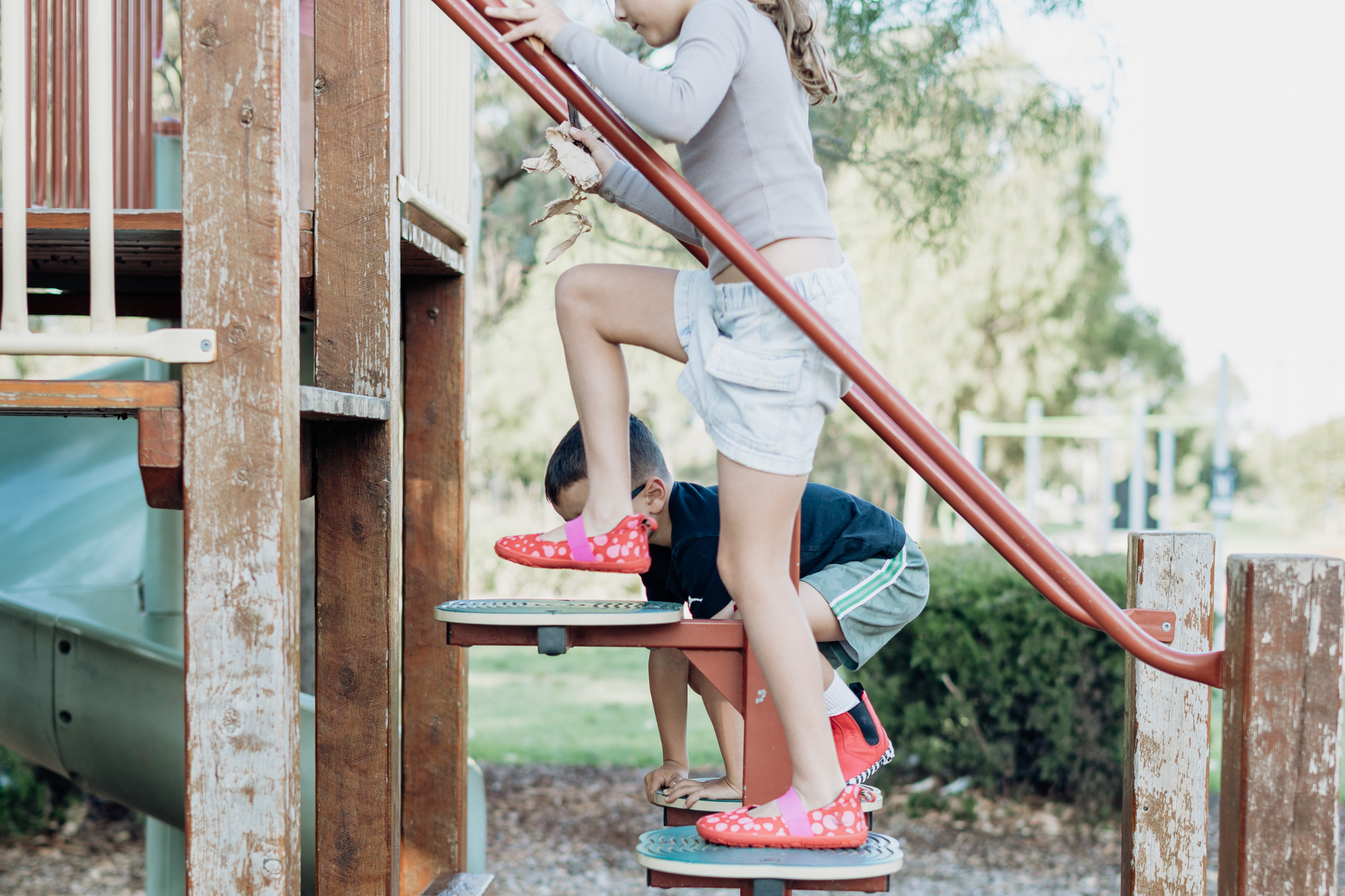 Children wearing foot-shaped red leather PaperKrane shoes on a playground.