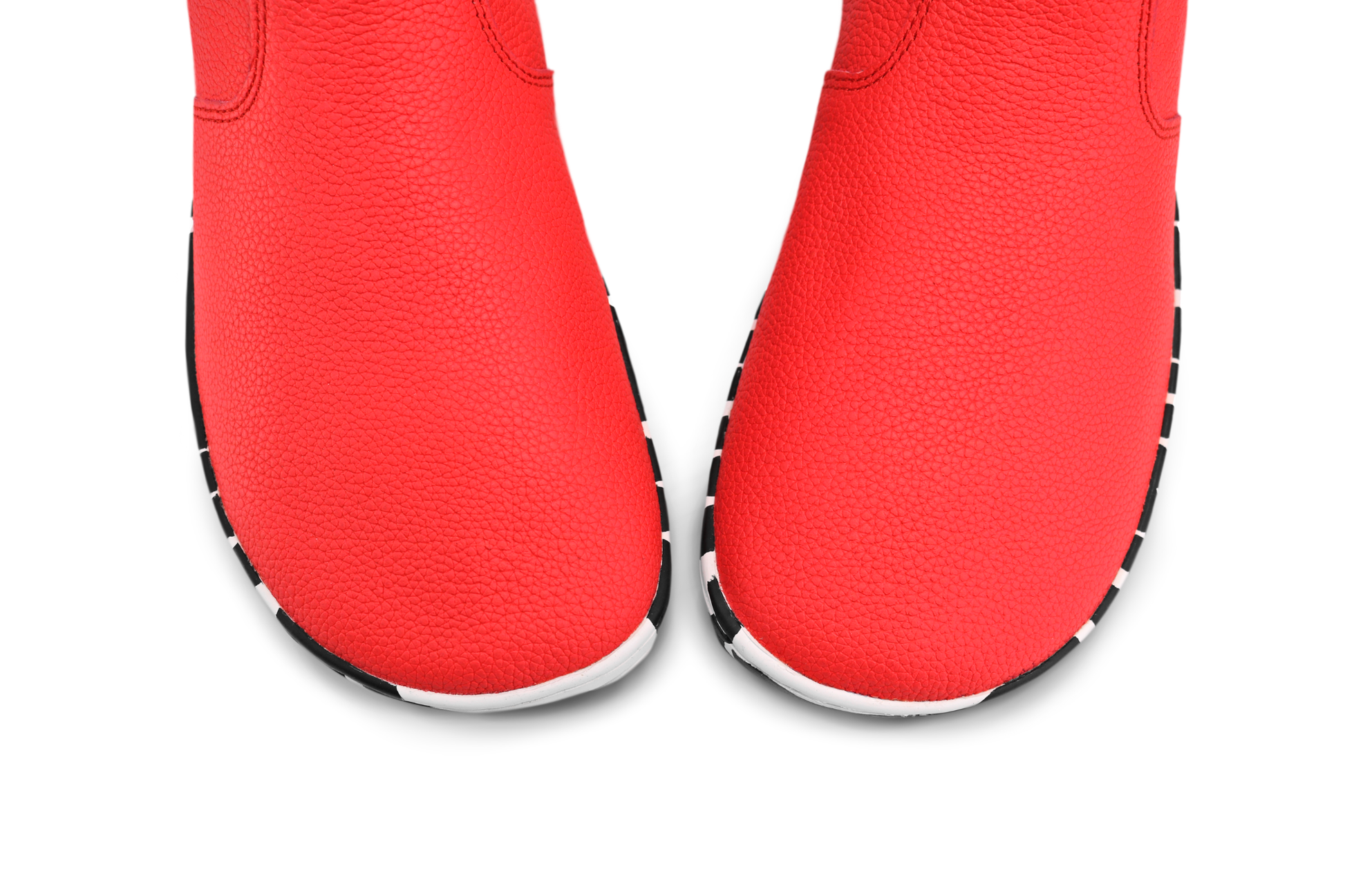 View from above the foot-shaped toe box of red leather PaperKrane barefoot chelsea boots with a zebra print rubber sole, on a white background. 