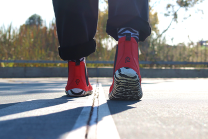 A person with black pants is walking away in red leather PaperKrane barefoot chelsea boots with a zebra print rubber sole. They're on a court.