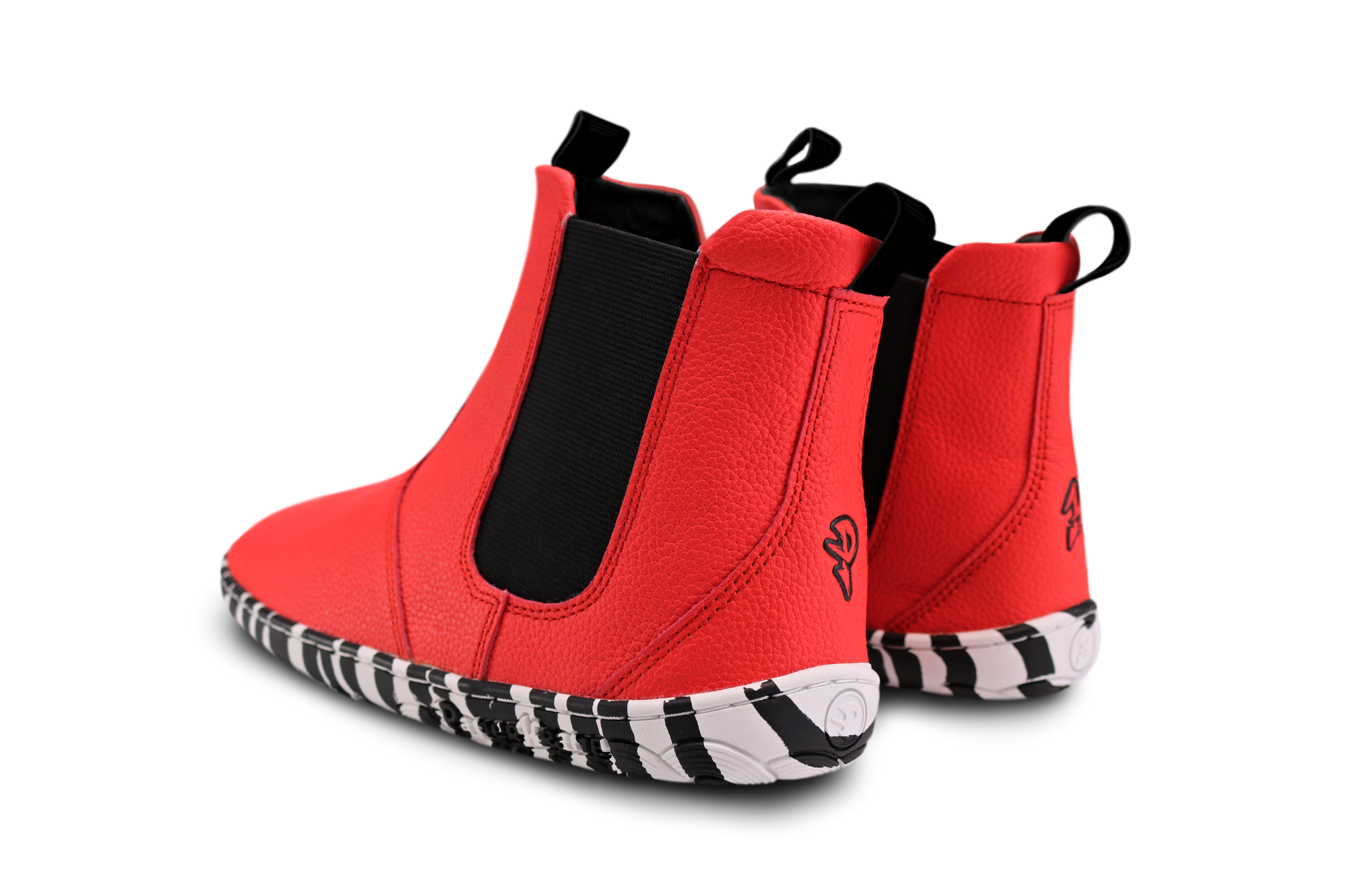 Back view of a pair of red leather PaperKrane barefoot chelsea boots with a zebra print rubber sole, on a white background. 