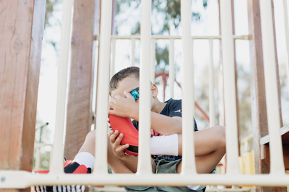 A child sits up high on a playground fort, and inspects the zebra print rubber sole of his foot-shaped red leather PaperKrane chelsea boots. 