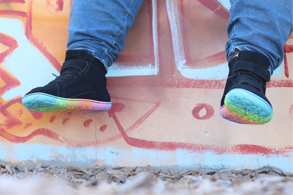 Black sneakers with colourful soles on a colourful concrete surface