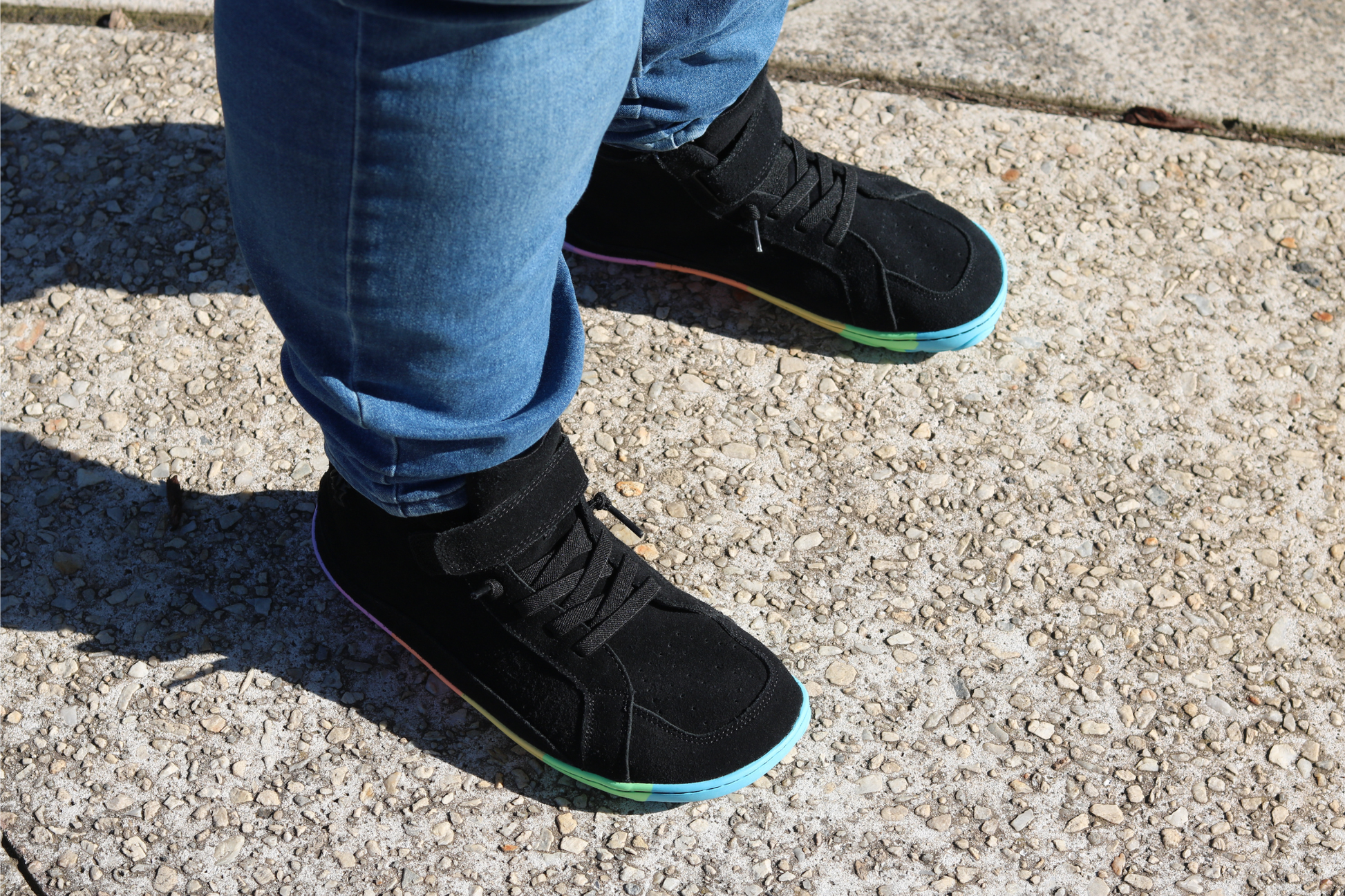 Person wearing black shoes with rainbow soles on a concrete surface