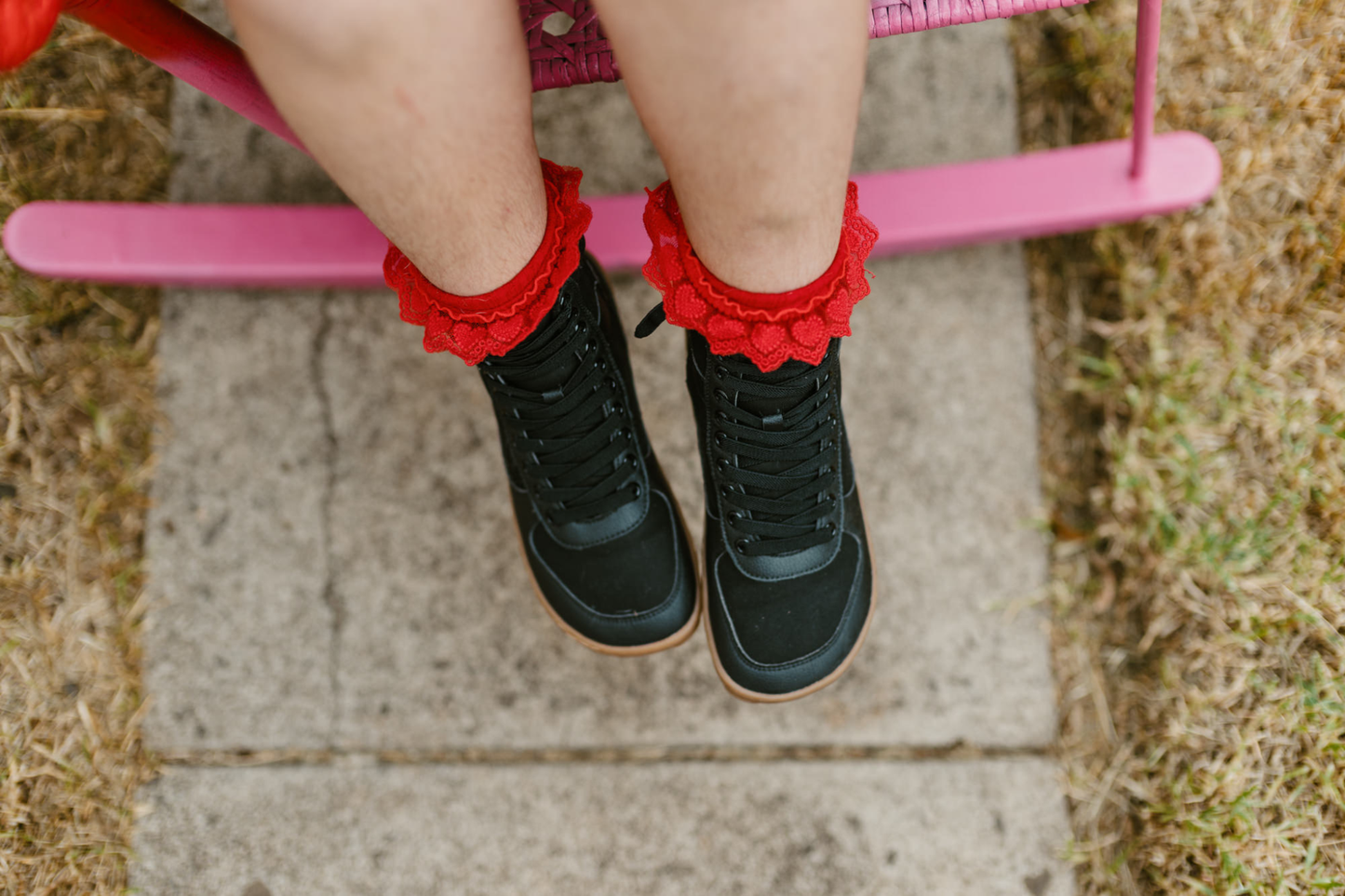 Above view of a child in red frilly socks sitting on a pink chair wearing black vegan foot-shaped SNUGG boots. 