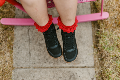 Above view of a child in red frilly socks sitting on a pink chair wearing black vegan foot-shaped SNUGG boots. 