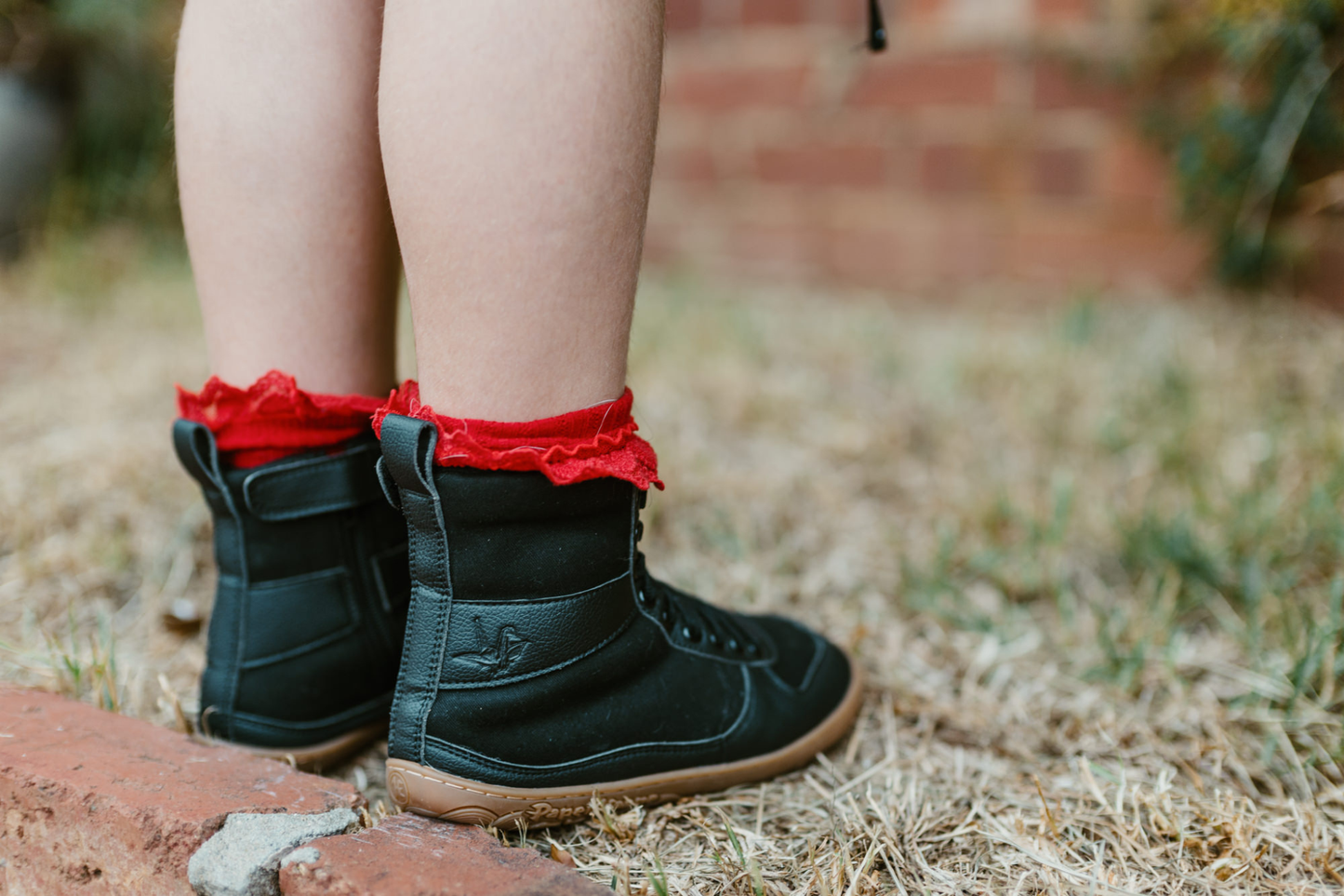 Back view of a child in red frilly socks in PaperKrane barefoot style SNUGG boots. You can see the embossed krane on the side. 