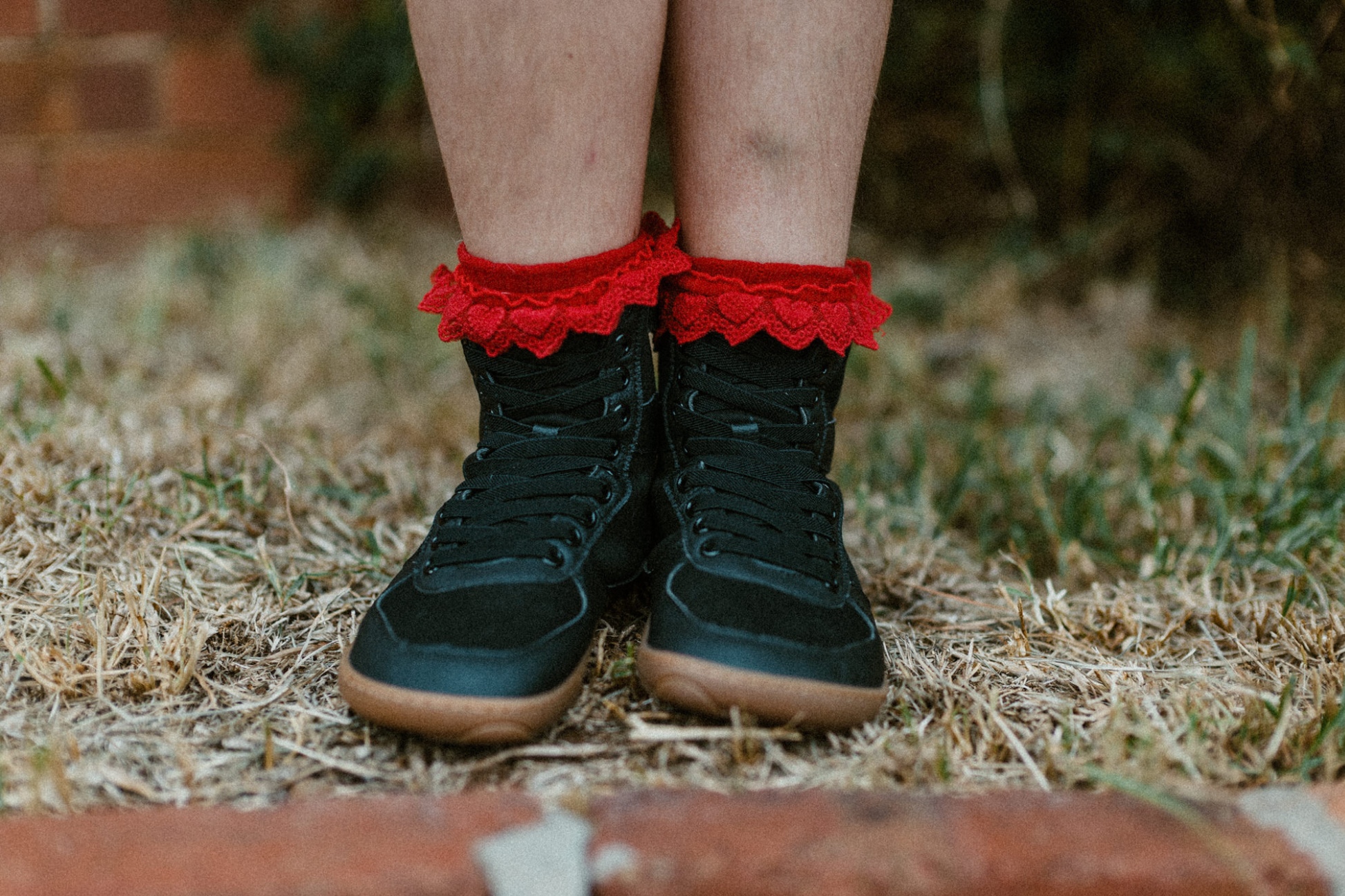 Front view of a child wearing red frilly socks and foot-shaped PaperKrane SNUGG boots. The boots are tall and have elastic laces. 