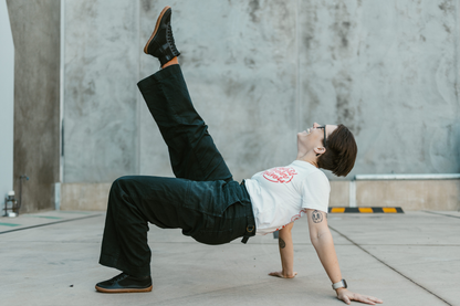 And adult joyfully kicks her leg into the air while wearing PaperKrane barefoot boots. They're vegan friendly, and have elastic laces and a zip on the inner ankle. The adult is creating a bridge with their body on a concrete floor.