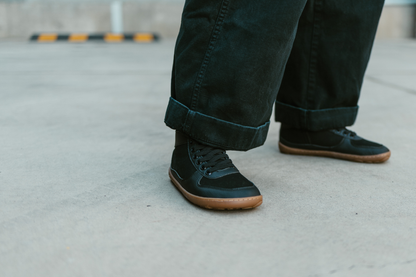PaperKrane SNUGG boots on concrete. The foot-shaped boots are vegan with elastic laces and a gum sole, the person is wearing black pants. 