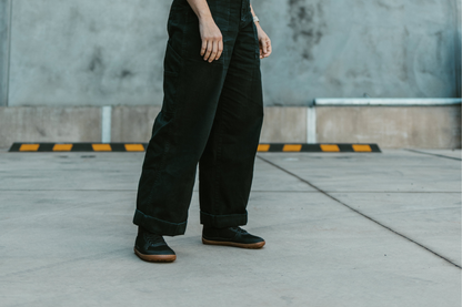 An adult wears PaperKrane vegan SNUGG boots on a concrete background. They're wearing black pants with the black boots. 