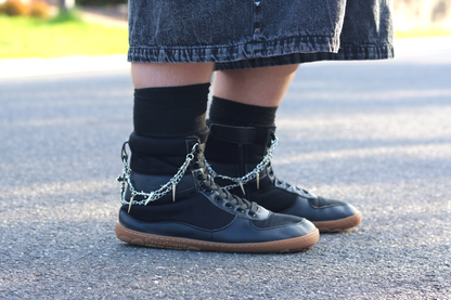 SNUGG boots with some personal accessories attached - silver chains. This is a great way to personalise your pair, or make them look a bit more alternative looking. The person has black socks with their black SNUGG boots and some black denim shorts, on a road. 