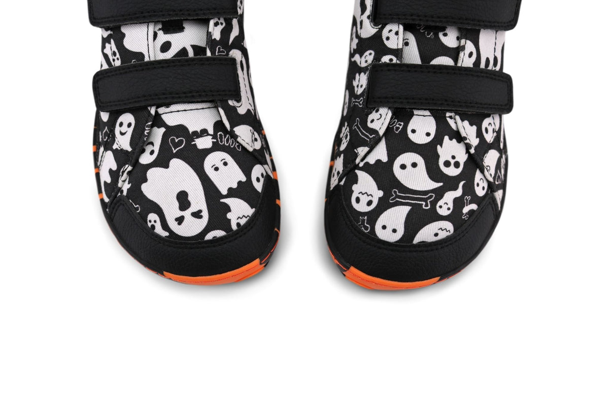 A pair of velcro sneakers from PaperKrane. These foot-shaped shoes have a black and white ghost print upper, with orange and black striped soles. On a white background and viewed from above. 