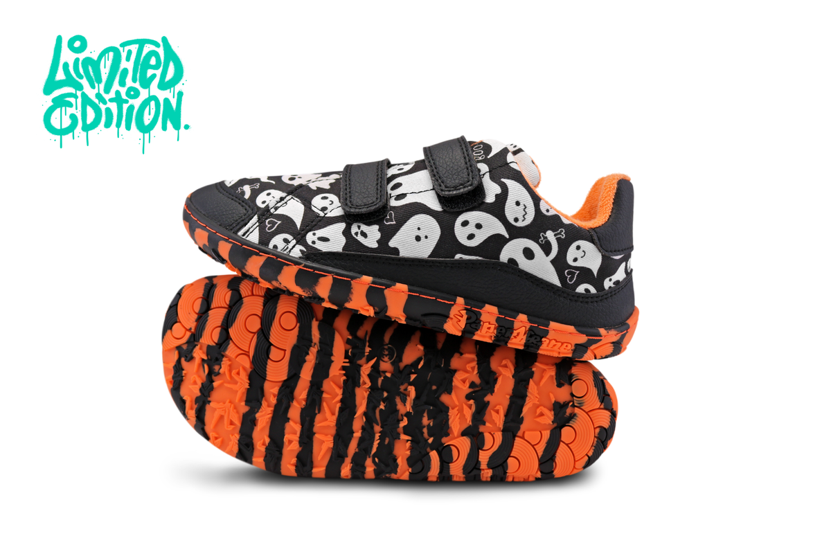 A pair of children's barefoot low-top velcro sneakers with a black and white ghost pattern upper and bright orange tiger-stripe soles, shown on a white background with a teal 'Limited Edition' graphic in the top left.