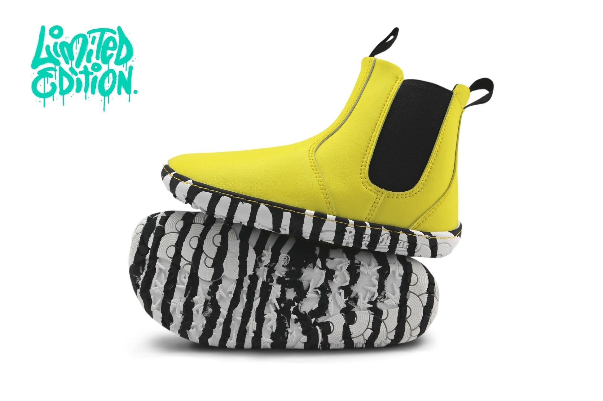 A bright yellow Chelsea-style foot-shaped ankle boot with black elastic side panels, shown resting on top of a black-and-white patterned shoe sole against a white background. A turquoise 'Limited Edition.