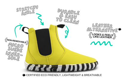 A bright yellow chelsea boot with a black elastic side panel and a black-and-white zebra-stripe sole, shown on a white background with hand-drawn callouts describing features like stretchy ankle, durable and easy to clean, leather alternative, non-removable micro suede inner sole, and certified eco friendly, lightweight & breathable.