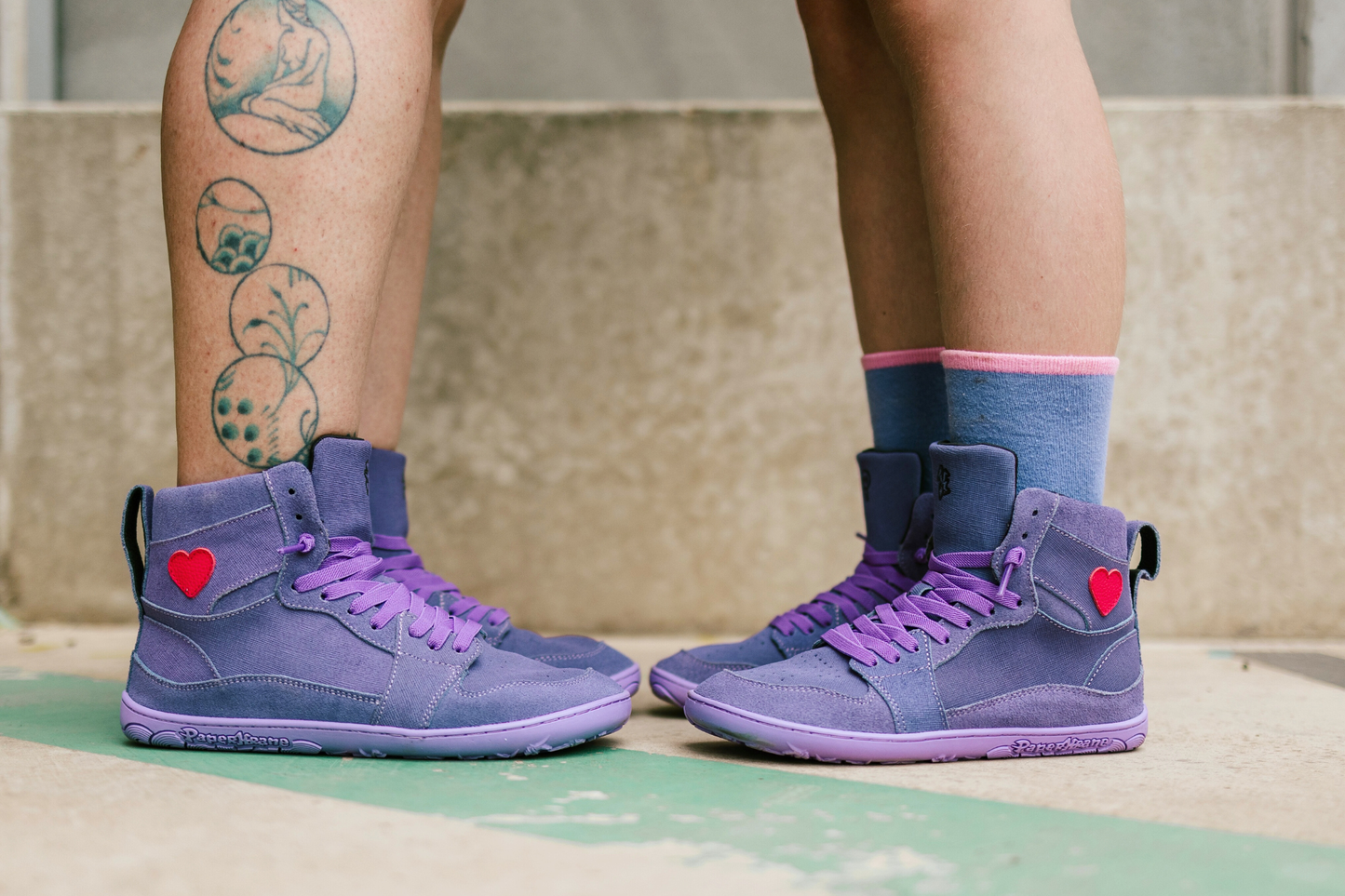 Purple high-top sneakers with heart details worn by two people on a concrete surface.