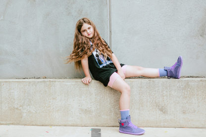 Young girl sitting on a concrete ledge wearing black outfit and purple boots.
