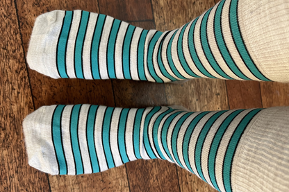 Pair of Roam Barefoot New Zealand made merino socks with teal and beige/grey stripes on a person's feet, on a wooden floor. 