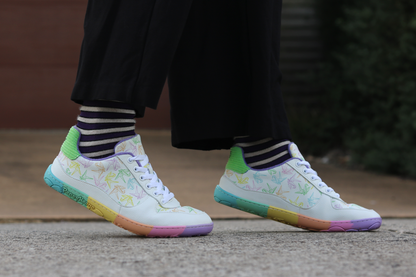 White barefoot sneakers from PaperKrane with a flexible foot-shaped rainbow sole, and rainbow origami cranes printed on them. 
Worn by a person with purple and beige striped merino socks from Roam Barefoot. Raised up on their toes. 