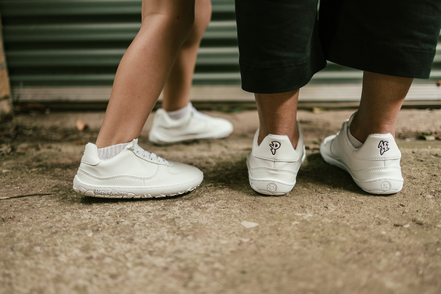 Two pairs of feet (CHILD AND ADULT) wearing white sneakers on a concrete surface.